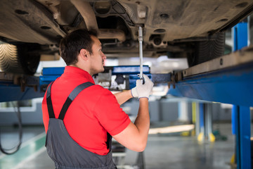 Car man mechanic examining car suspension of lifted automobile at repair service station