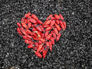 Obraz na płótnie Canvas Red birds eye chili in the shape of a heart on black stone background, close up