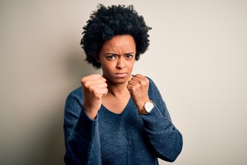 Fototapeta na wymiar Young beautiful African American afro woman with curly hair wearing casual sweater Ready to fight with fist defense gesture, angry and upset face, afraid of problem