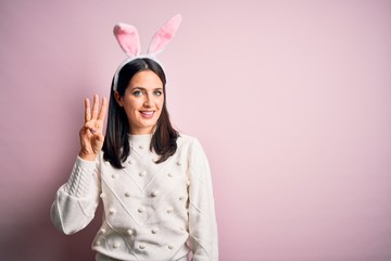 Young caucasian woman wearing cute easter rabbit ears over pink isolated background showing and pointing up with fingers number three while smiling confident and happy.