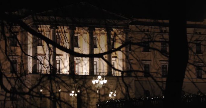 Cinematic slow motion medium wide 4K shot with parallax motion of the illuminated royal palace and the iconic balcony on top of Karl Johan street at night, in Oslo Norway.