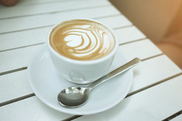 A cup of coffee with heart pattern in a white cup on white wooden background