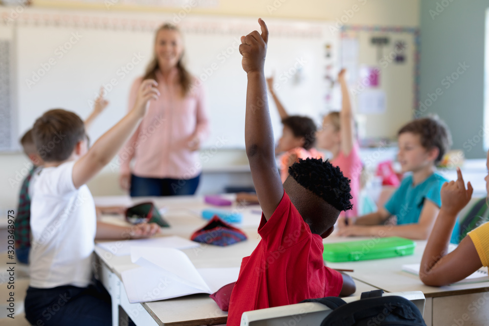 Wall mural group of schoolchildren raising their hands in an elementary school classroom