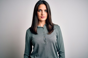 Young brunette woman with blue eyes wearing casual green sweater over white background with serious...