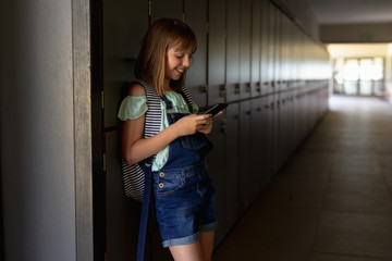 Schoolgirl leaning against lockers in a corridor using a smartphone