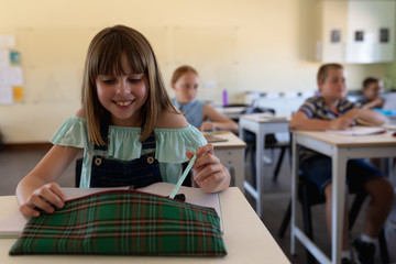 Schoolgirl sitting at a desk taking a pen from her pencil case