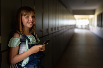schoolgirl leaning against lockers in a corridor using a smartphone
