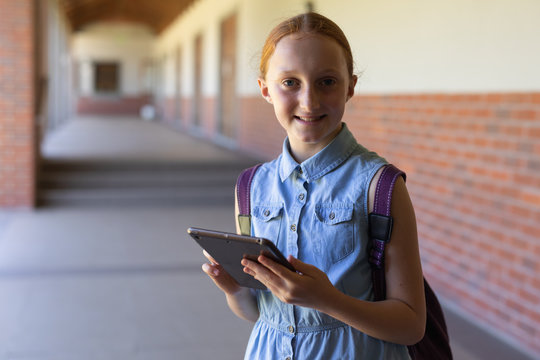 Schoolgirl standing in the schoolyard at elementary school using a tablet computer