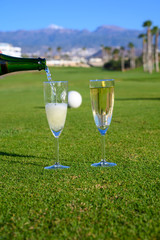 Two glasses with  bubbles white champagne or cava wine served on green golf club grass with mountains view during golf competition event or celebration