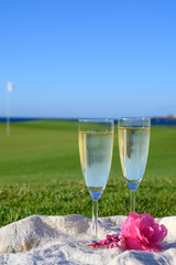 Two glasses with bubbles white champagne or cava wine served on green golf club grass with sea view for romantic event or celebration