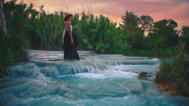 4K UHD Cinemagraph / seamless video loop of a young woman standing in a thermal hot springs waterfall in Saturnia, Italy. The warm blue water is endlessly flowing around her. Video Schleife.