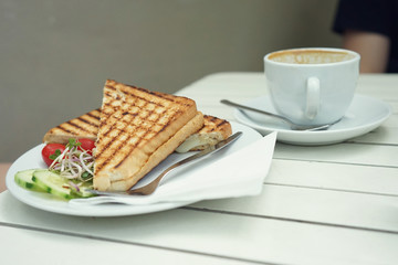 Club sandwich with cheese and cherry tomato on white wooden table.