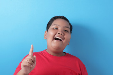 Happy fat Asian boy pointing finger up, having idea gesture