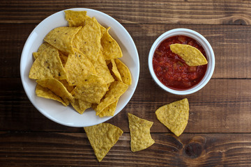 Tortilla chips inside bowl with salsa on rustic wooden table top