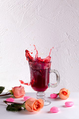 Glass of red wine with roses and hearts on white background.
