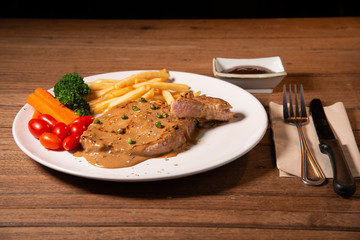 Big steak, french fry, pepper, little tomato, slice carrot, broccoli and BBQ sauce with fork, knife, tissue paper on wood table stock photo