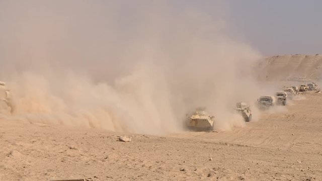 A military column of armored vehicles moves through the desert, raising dust. Special operation of the military.