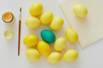 Above view of pastel yellow Easter eggs with green accent and paint brush arraigned in minimal composition on white background, copy space