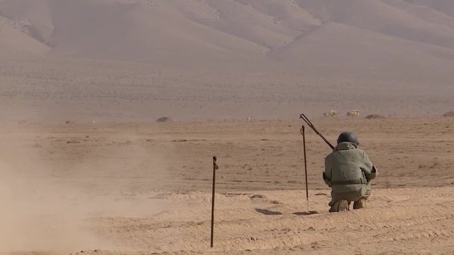 Military sappers in armored suits cleared the road in the desert, running away from the danger zone for an explosion