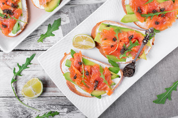 Sandwich with salted trout, avocado, cream cheese, black caviar and arugula on the white platter