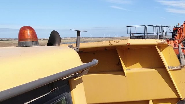 Action cam shot of a dumper truck being loaded by a large digger bucket with earth