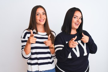 Young beautiful women wearing casual clothes standing over isolated white background pointing fingers to camera with happy and funny face. Good energy and vibes.