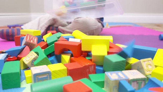 Toddler boy dumping a container of colorful blocks on to the floor.