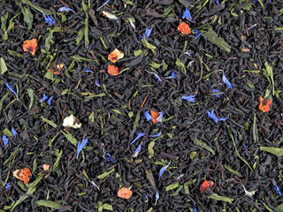 Tea mix of green and black varieties with pieces of wild strawberry and cornflower flowers, natural background of dry tea leaf  