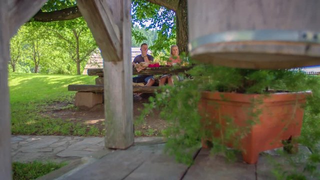 Dolly wide shot behind pillar, Couple sit and eat outdoors on table, Low angle selective focus