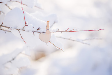 wooden heart hanging on a clothespin on a snow branch, glare . The concept of Valentine's Day .