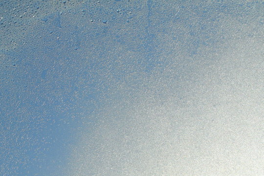 Blue window glass covered hoarfrost ice pattern texture with water drops. Cold nature winter background