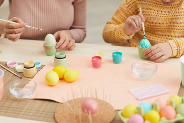 Obraz na płótnie Canvas Close up of mother and daughter painting Easter eggs pastel color sitting at table in cozy kitchen interior, copy space