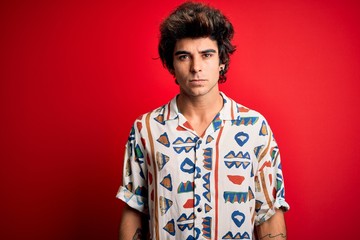 Young handsome man on vacation wearing summer shirt over isolated red background Relaxed with serious expression on face. Simple and natural looking at the camera.