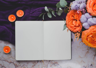 Artist mockup. Blank sketchbook, orange roses and candels, purple cotton on marble background