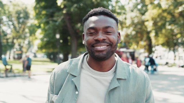 Portrait of cheerful african american man stands in city street smile happy sunset young attractive face positive sunlight city fashion outdoor close up slow motion
