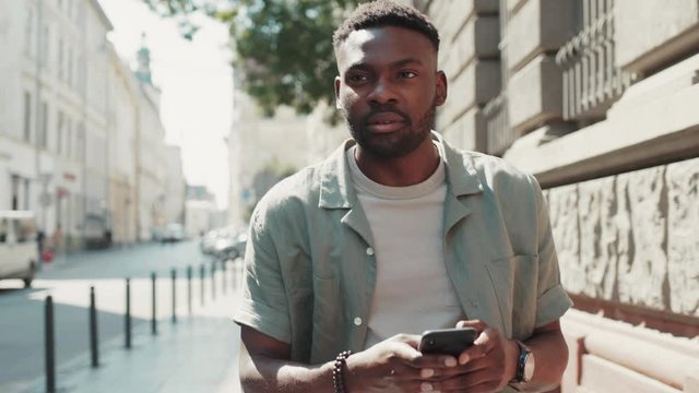 Handsome stylish african american young attractive man using phone walk on street smile sunlight sunset cellphone fashion internet face outside technology businessmen black young city mobile close up