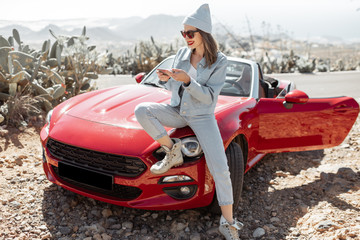 Young woman dressed casually with hat enjoying road trip on the island, standing with phone near...