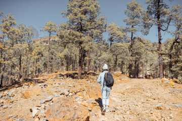 Young woman dressed casually walking with backpack in the forest highly in the mountains on the volcanic rocks, traveling on Tenerife island, Spain