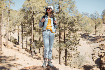 Portrait of a stylish woman enjoying beautiful landscapes on volcanic rocks in the pine woods, traveling high in the mountains on Tenerife island, Spain