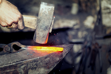 Blacksmith working metal with hammer on the anvil