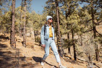 Naklejka premium Young woman dressed casually walking with backpack in the forest highly in the mountains on the volcanic rocks, traveling on Tenerife island, Spain