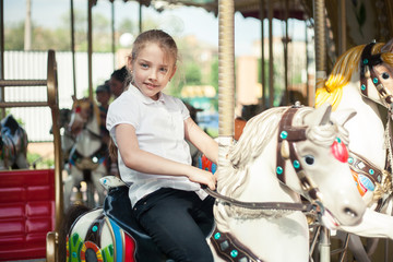 A girl riding a toy horse on a carousel in the park.