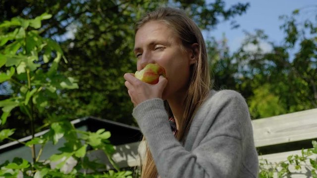 Girl takes bite from apple and stares out on windy day, low angle