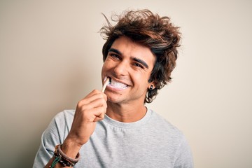 Young handsome man smiling happy. Standing with smile on face whasing tooth using toothbrush over isolated white background