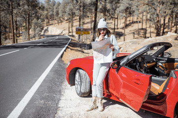 Woman enjoying road trip, standing with map near convertible car on the roadside in the volcanic mountain forest on Tenerife island, Spain