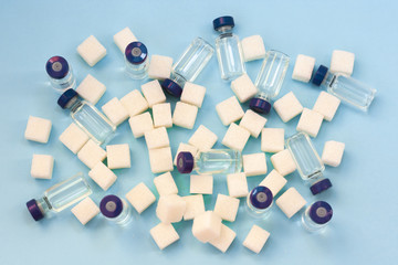 Sugar addiction, insulin resistance, unhealthy diet, sugar cubes and bottles of insulin on blue...