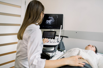Woman doctor conducts an ultrasound diagnosis of the patient abdomen and internal organs, looking at the screen of modern ultrasound machine. A girl lies on a couch in an ultrasound diagnostic room