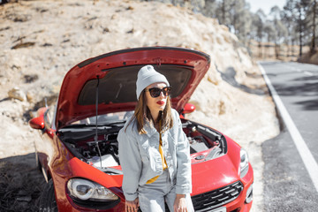 Frustrated woman standing on the roadside, having some problems with a car while traveling alone at the mountains