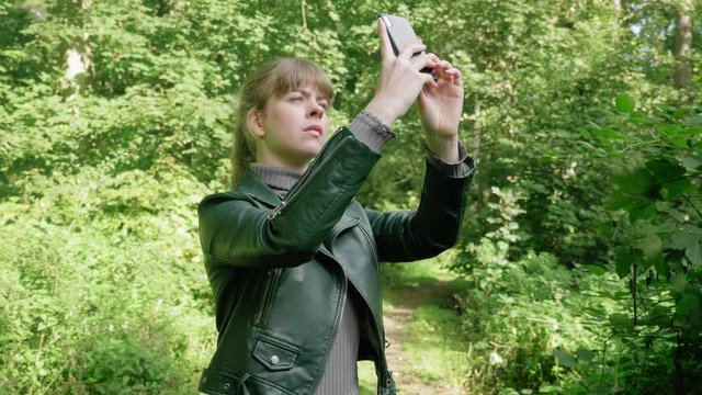 Girl points phone up with camera app for photo in woods, tracking