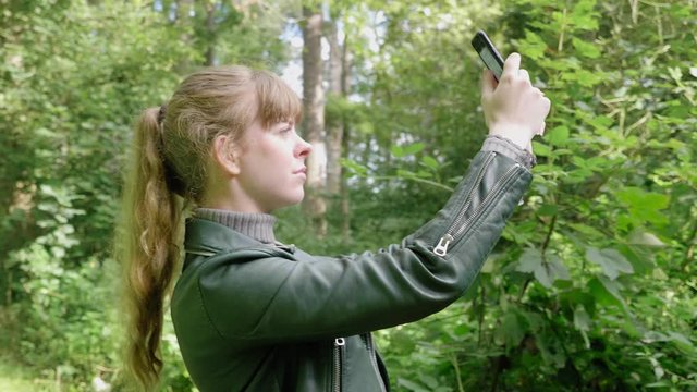 Girl holds up phone to take picture on bright day in woods, close-up